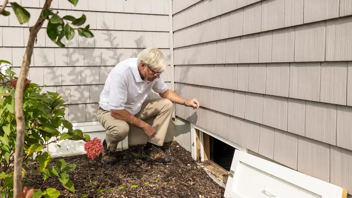 Home inspector opening the access hatch to a crawl space beneath a house